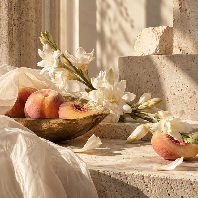 Editorial artwork for Amandine Clerc-Marie: peach skin, tuberose petals and architectural pale stone planes, warm delicate daylight.